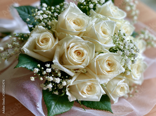 Beautiful bouquet of white roses with babys breath flowers wrapped in delicate fabric on a wooden surface