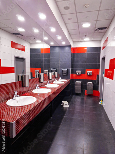 Modern public restroom interior with red mosaic counter, white sinks, and tiled walls.