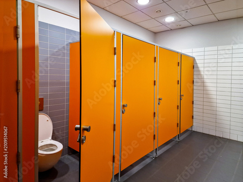 Modern public restroom interior with orange toilet cubicle partitions and ceramic tile walls.