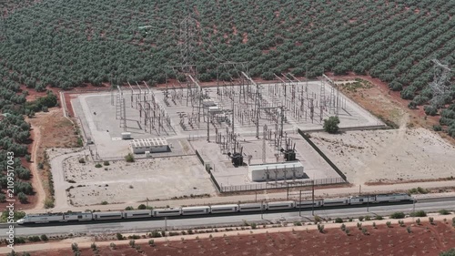 Aerial view of a high speed train traveling near a power grid station and olive groves in Spain