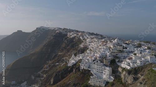 Aerial view of Fira, Santorini, with its whitewashed buildings clustered along the caldera rim above a winding switchback path down the cliffside.