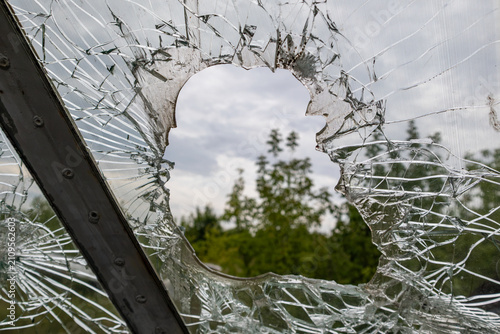 View through shattered glass window on green trees. Broken radial fracture fragmented, textured foreground