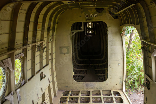 Interior of derelict weathered An-2 airplane aircraft, weathered metal and open cargo doors surrounded by green forest, hauntingly serene atmosphere