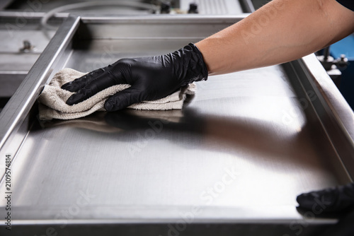 Fotografie Hand in black glove wiping down a shiny stainless steel surface with a cloth