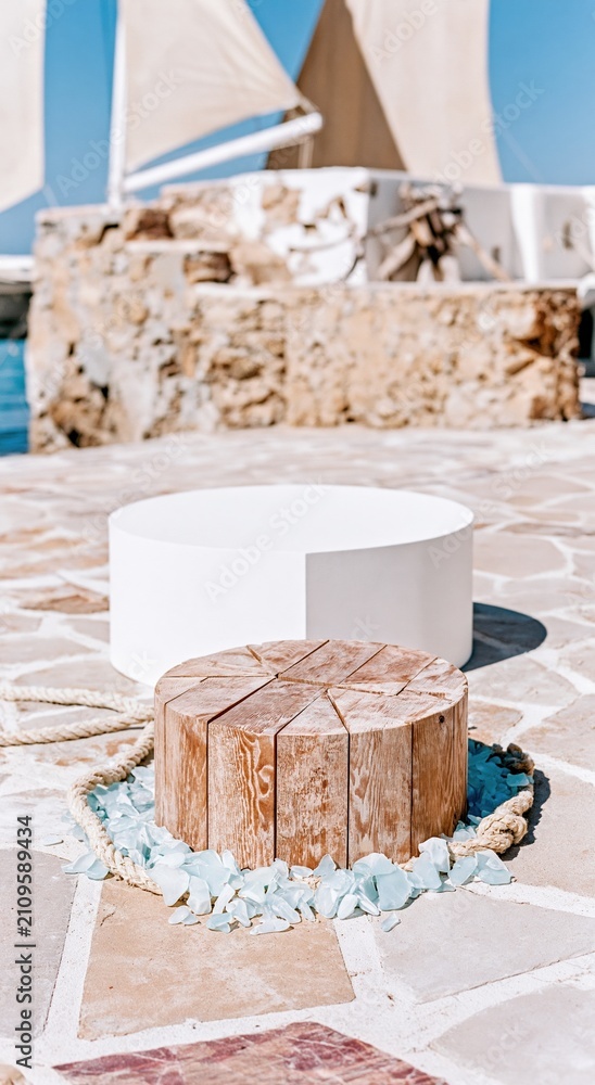 Fototapeta premium Circular wooden dock podium and white pedestal on a stone jetty for coastal product display, featuring weathered textures and sea glass