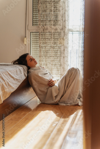 Foto Sad lonely female feeling down, sitting on bedroom floor wrapped in bedsheet