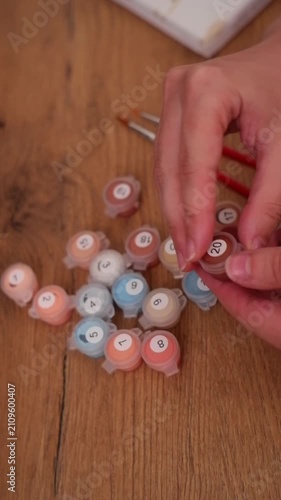 Woman's hands opening a small container of brown paint and dipping a brush in it for a hobby