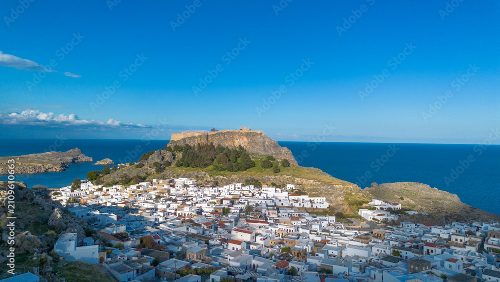 Obraz premium Panoramic view of the historical white houses in Lindos village with the Acropolis on the cliff and deep blue sea on Rhodes island Greece