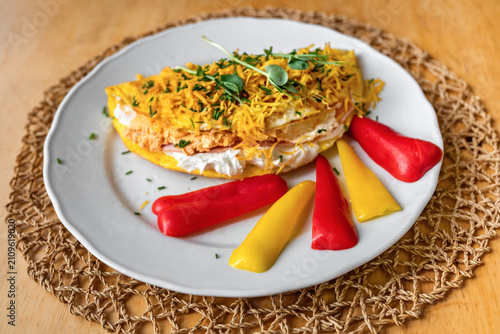 Egg omelette with white cheese filling, sprikled with cheese and herb, sliced red anyd ellow pepper