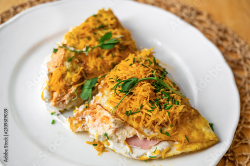 Omelette with fresh white cheese and ham, sprinkled with grated cheese and herb.