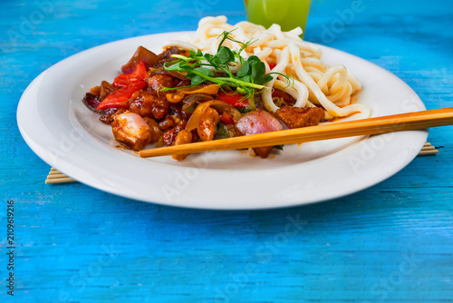 Foto Spicy kung pao with udon noodle, chopstick on white plate on blue background