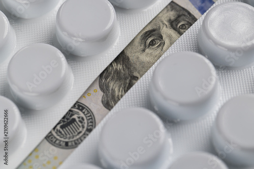 Benjamin Franklin portrait on 100 dollar bill visible between medicine blister packs