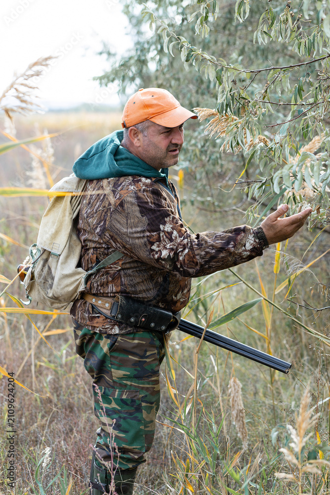 Fototapeta premium A hunter with a gun in camouflage clothing. A senior man with a gun, medium shot, searching for game.