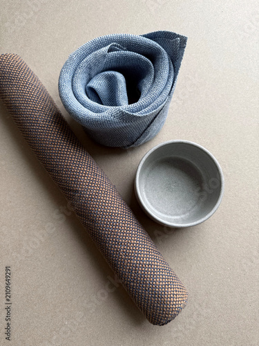 Rolled linen napkins and a small ceramic cup in a minimalist composition. Natural textile textures and handmade stoneware create a calm still life for home decor, dining and interior styling.