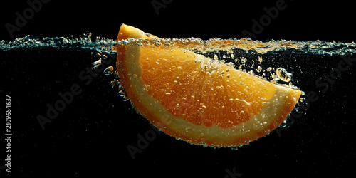 A slice of orange falling into the water with bubbles and splashes