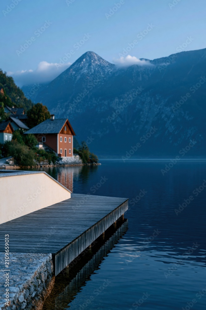 Fototapeta premium Wooden corner pier beside quaint lakeside houses with mountain peaks for calm wallpaper and banner background