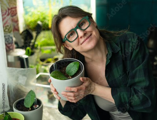 Cuadro en lienzo A joyful woman holds a potted plant seedling and smiles in a sunny room at home