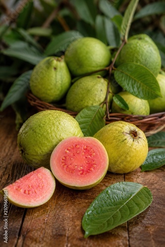 Fresh pink guava fruits with sliced guava and green leaves on rustic wooden table background
