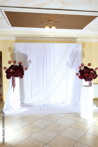 Photography Elegant wedding photo backdrop with white drapery, burgundy floral arrangements and stylish reception hall decoration