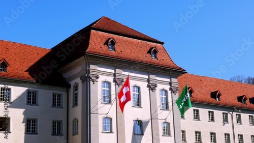 Old Building with Swiss Flag and St Gallen Canton Flag Waving in the Wind with Blue Sky in a Sunny Day in City of St Gallen, St Gallen Canton, Switzerland.