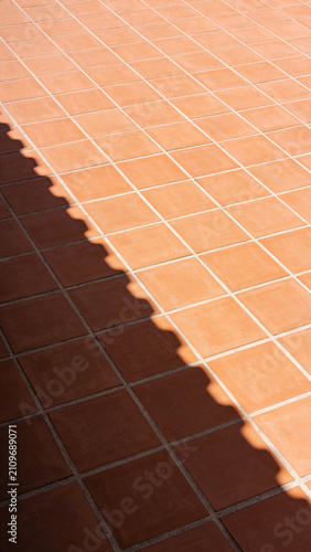 Terracotta roof tiles casting a strong geometric shadow on a Mediterranean patio floor in sunny weather