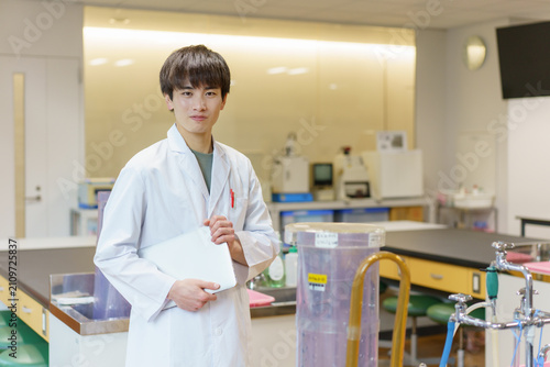 ノートパソコンを持って立つ若い男性研究員のポートレート　撮影協力：学校法人電波学園　東京電子専門学校