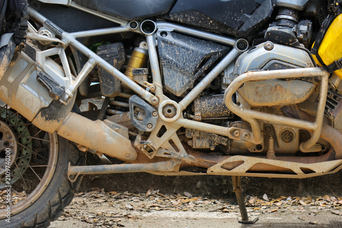Muddy adventure motorcycle engine and frame close up showing dirt covered suspension, exhaust, skid plate and rear wheel, rugged touring bike worn from off road travel