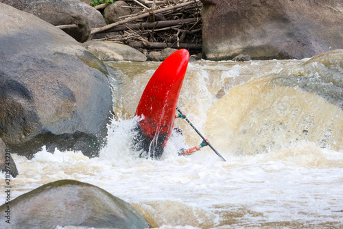 Canvastavla Red kayak capsized in turbulent river rapids near boulder with paddler submerged