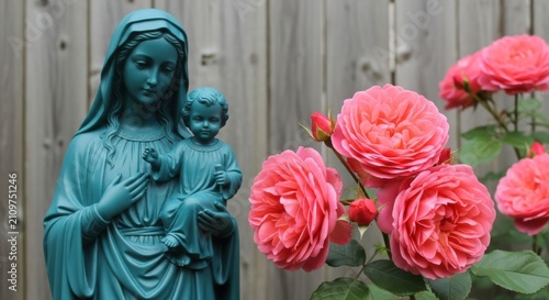 Blue statue of virgin mary holding baby jesus with blooming pink roses in a garden