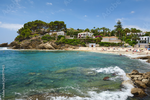 Cala de la Fustera beach with clear turquoise Mediterranean water, rocky coastline, coastal villas and summer visitors on the Benissa coast near Calpe, Spain