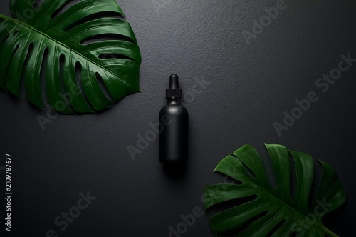 Black cosmetic dropper bottle with monstera leaves on dark textured surface cosmetic skincare monstera branding wellness essential treatment packaging container botanical dermatology