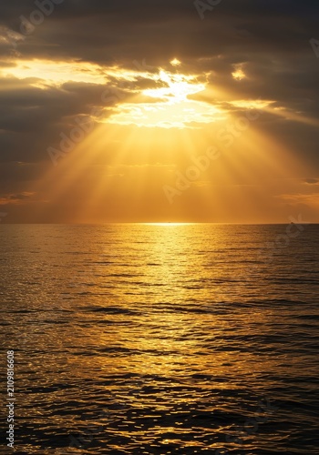 Golden sunlight beams pierce through the cloudy sky, illuminating a tranquil ocean surface at sunrise or sunset, creating a dramatic scene ,horizon ,cloud ,tranquil