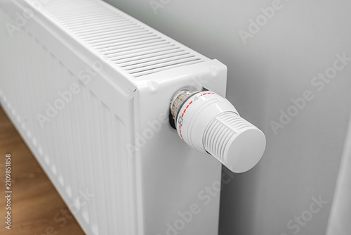 A modern white panel radiator with a thermostatic temperature control valve mounted on an interior wall.