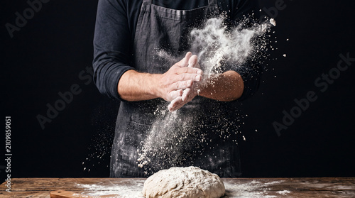 Extreme close-up of artisan baker hands sprinkling flour over raw yeast dough with rustic bakery atmosphere.