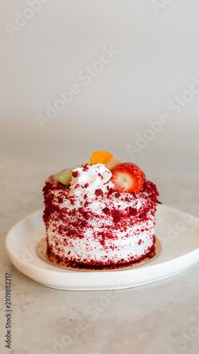 Obraz na płótnie Red Velvet Cake Delight: A single, exquisitely decorated red velvet cake sits on a white plate, topped with fresh fruits and creamy frosting, promising a delightful indulgence