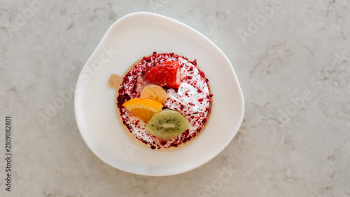 Konstfotografi Delightful Fruit Tart: A vibrant and delectable fruit tart is presented on a white plate, showcasing a colorful medley of fresh fruits atop a creamy base and a crisp pastry crust