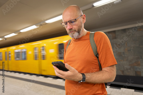 Person using smartphone on subway platform near yellow train
