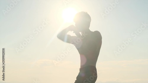 Young muscular fighter trains shirtless alone at sunset, practicing an elbow strike during shadow boxing. MMA, self defense, martial arts training, personal safety and confidence.