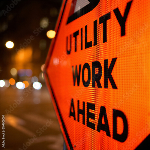 Utility work ahead warning sign illuminated at night in urban area  