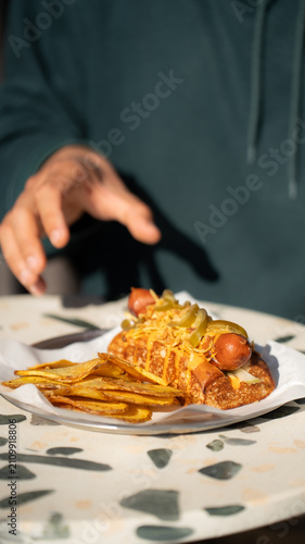 Slika na platnu Gourmet Hot Dog Feast: A delicious gourmet hot dog, smothered in melted cheese and topped with pickles and onions, is served with a side of crispy potato chips