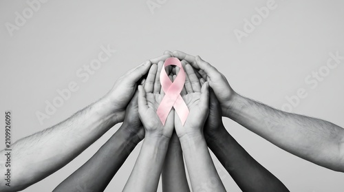 Group of diverse people holding pink awareness ribbon together in cupped hands for medical solidarity.