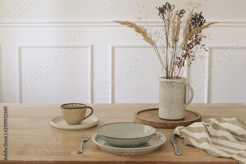 Foto Minimalist Wooden Table Setting with Ceramic Dinnerware, Dried Flowers Grass in Jug Vase