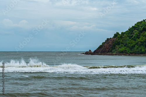 Bild auf Leinwand Crashing ocean waves against the coast with a green rocky headland under a cloud
