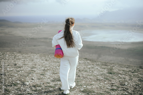 Back view of a woman carrying a yoga mat walking in nature