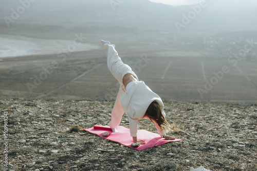 Woman practicing three legged downward facing dog yoga pose outdoors