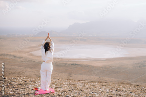 Back view of a woman meditating with raised arms in a vast landscape