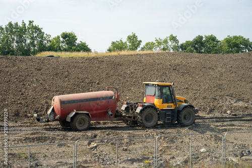 Canvas Print Tractor pulls red water tank across ploughed construction field