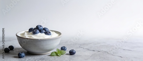 Fresh yogurt bowl with blueberries and mint leaves on minimalist white surface