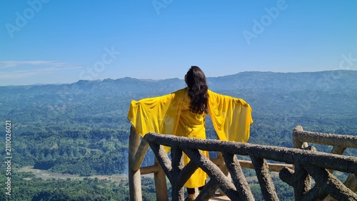 Foto Woman in yellow dress standing on a mountain balcony overlooking a vast valley d
