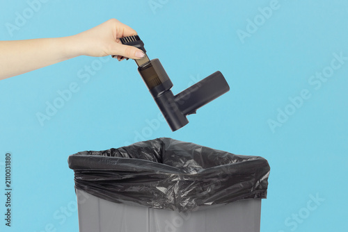 Throwing a portable cordless mini vacuum cleaner with brush nozzle into the trash can, holding a mini vacuum cleaner in hand front of the trash can